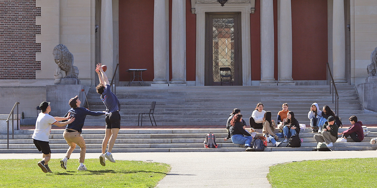 Bowdoin students toss a football in front of the steps of the Art Museum.