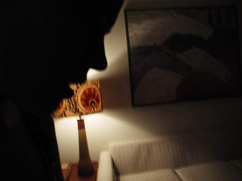 A profile of a woman's face in a darkened room with a lamp behind her