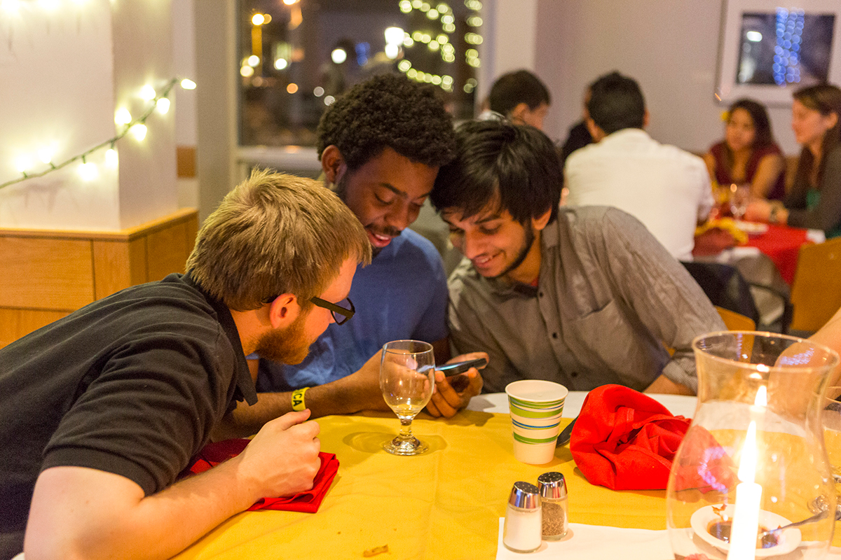 Three students at a party discuss a photo on a phone.