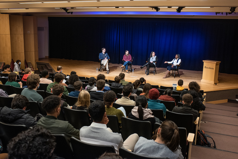 Four people on a stage before a large crowd