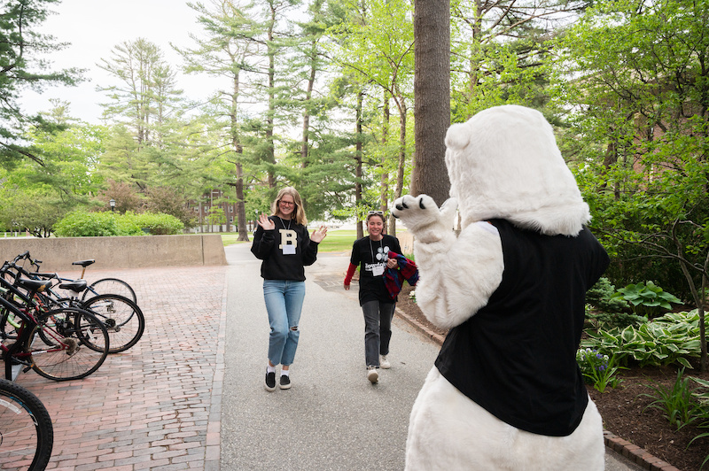 Two people walking towards Bowdoin polar bear mascot