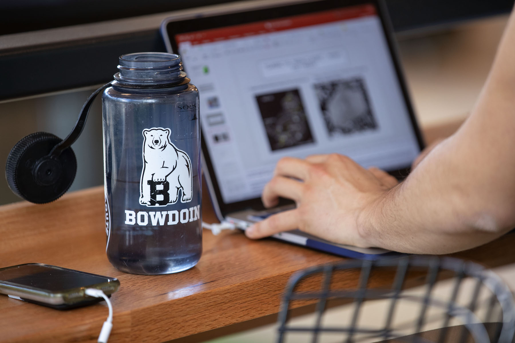 Image of plastic water bottle with Bowdoin polar bear logo next to student working on laptop. 