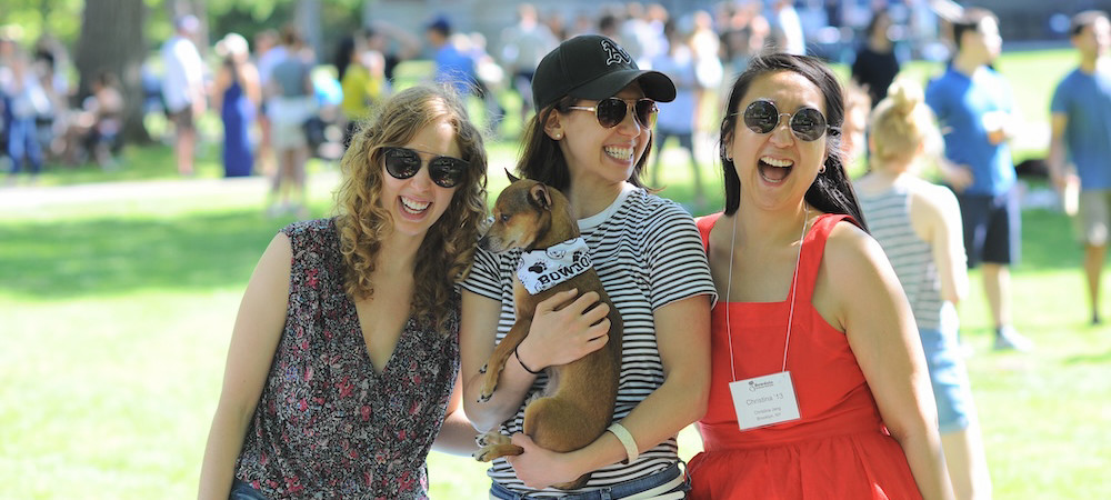 Three people, one hold a dog, laughing