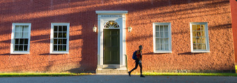 A Bowdoin student walks in front of Massachusetts Hall.