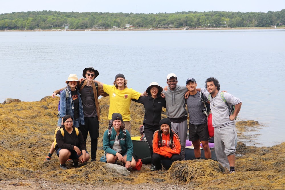A large group of students posing for photo with body of water behind them