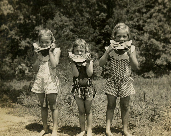 An old photograph showing three girls eating watermelon
