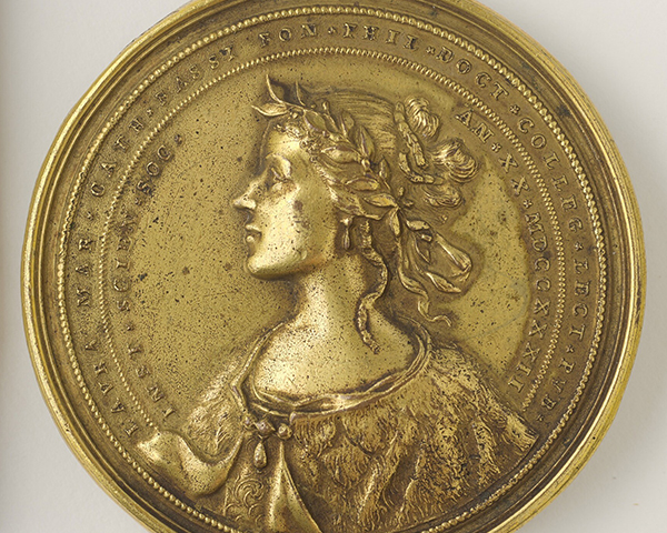 A historic medal in a golden color showing the profile of a woman