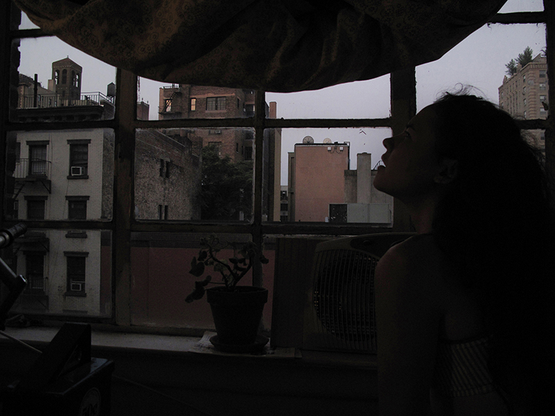 a photograph of a woman's face in half profile in a darkened room in front of a window