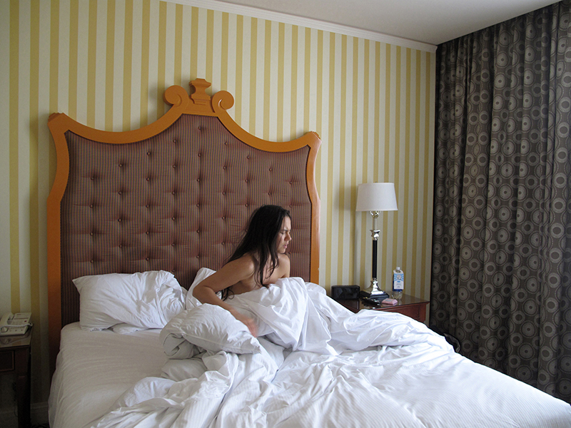  A photo of a woman sitting in a bed in front of yellow striped wallpaper