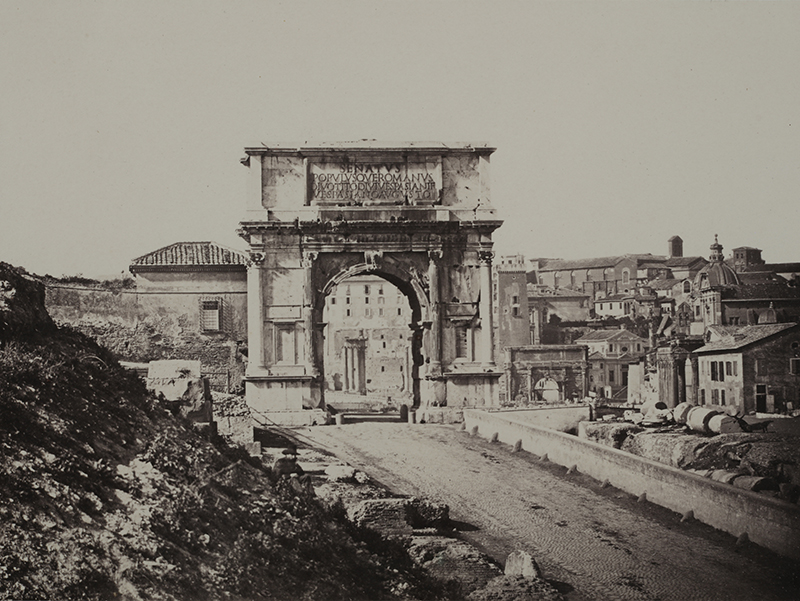 A sepia photograph with a road leading to an large architectural arcch
