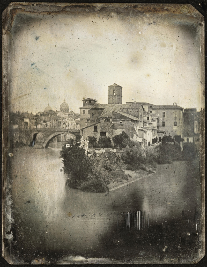 An old photograph showing water in the foreground, with a town in the background