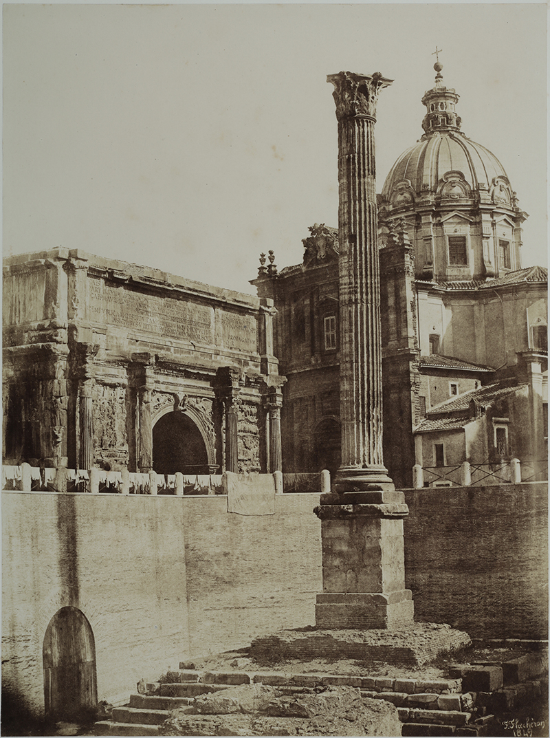 A sepia photograph with steps leading to an obelisk, a wall on the left, and a domed building in the background