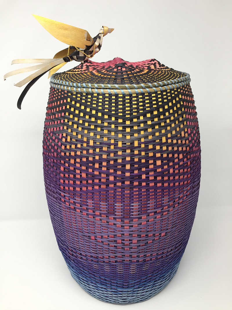 A colorful, woven basket with a woven bird on the lid. 