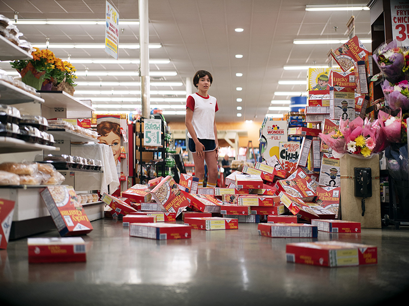 A girl standing in a supermarket among boxes of the cereal "Lucky Charms" that have fallen on the floor