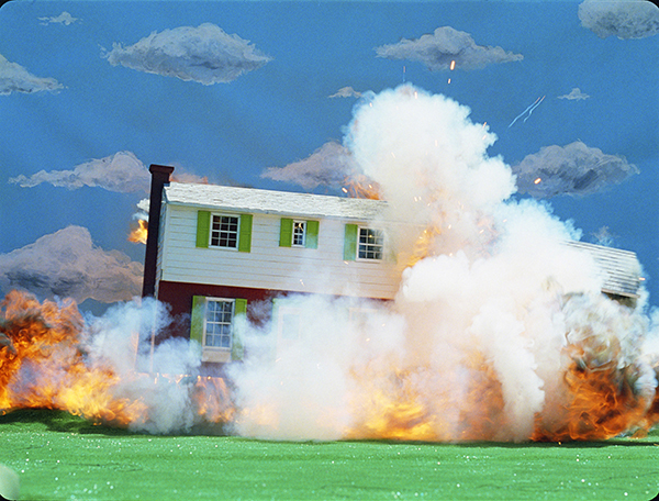 A white and red house with bright green shutters being lifted off the ground by an explosion of fire and smoke