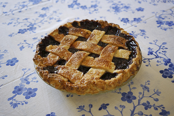 A fruit pie with a lattice crust on a tablecloth with a blue floral pattern