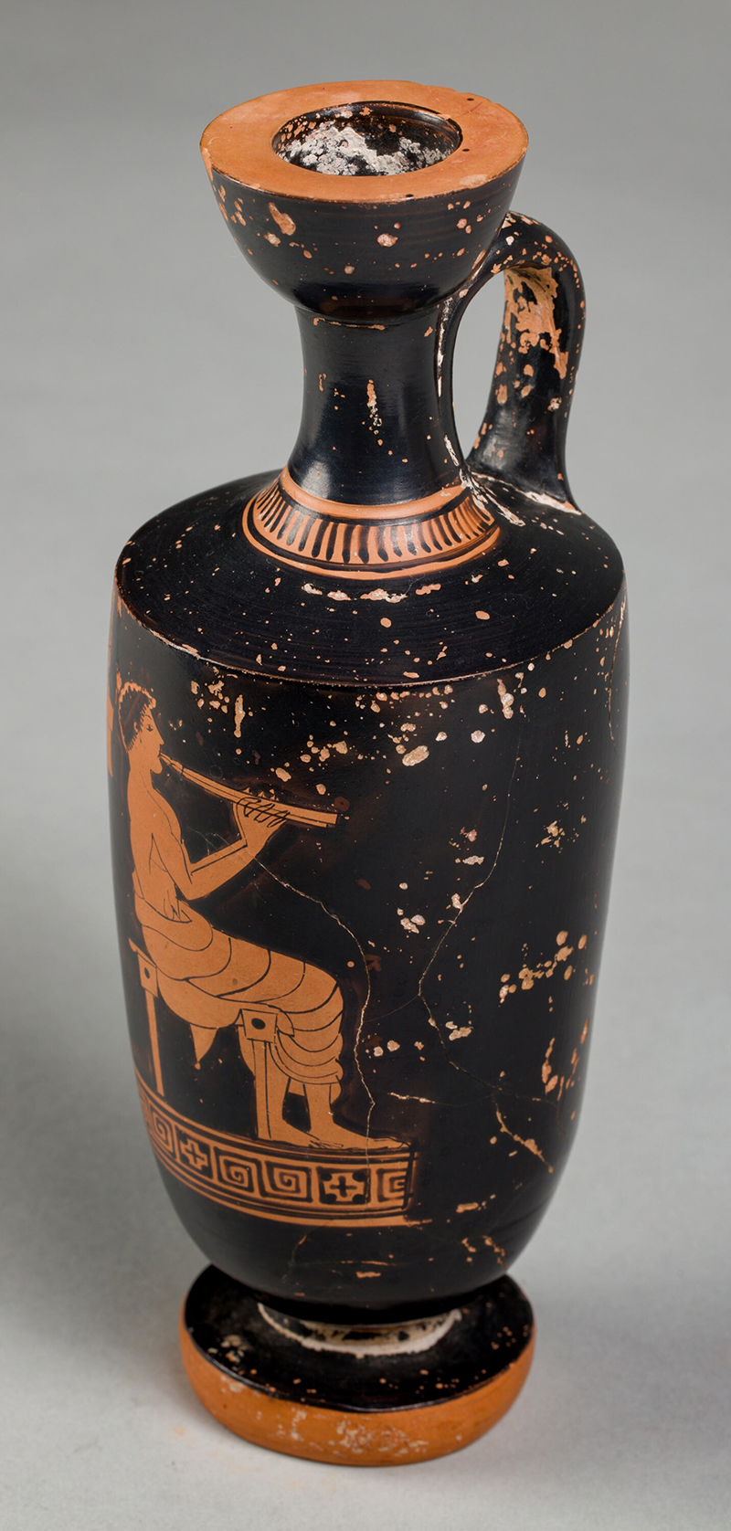 An ancient red figure vessel with a painting of a figure playing the flute