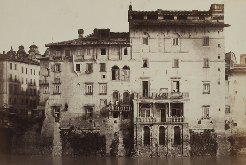 a sepia photograph of a large white, multi-storied building with many windows with a river at the foundation