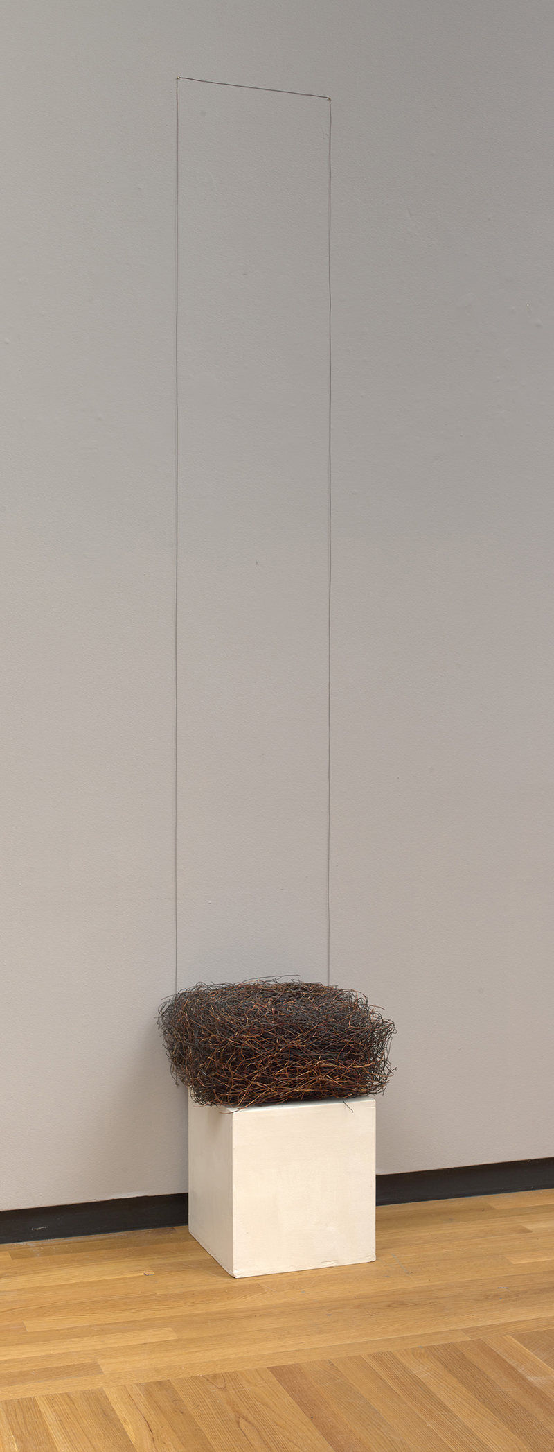 an installation view of a piece made with a  gathering of copper wire and nails with a white pedestal at the bottom, a 