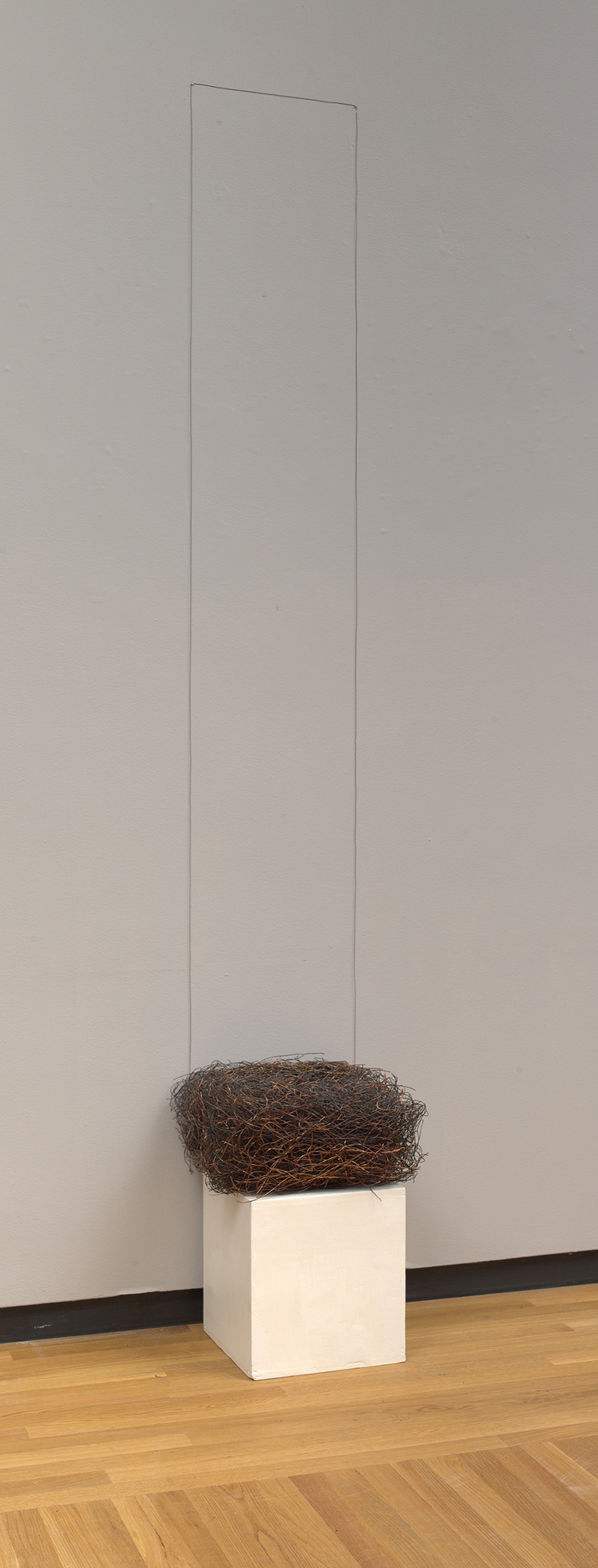 an installation view of a piece made with a gathering of copper wire and nails with a white pedestal at the bottom, a