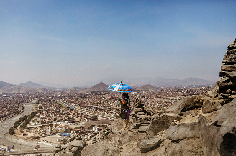 a photograph of a rocky landscape, with a cityscape in the distance,  and a person holding an umbrella