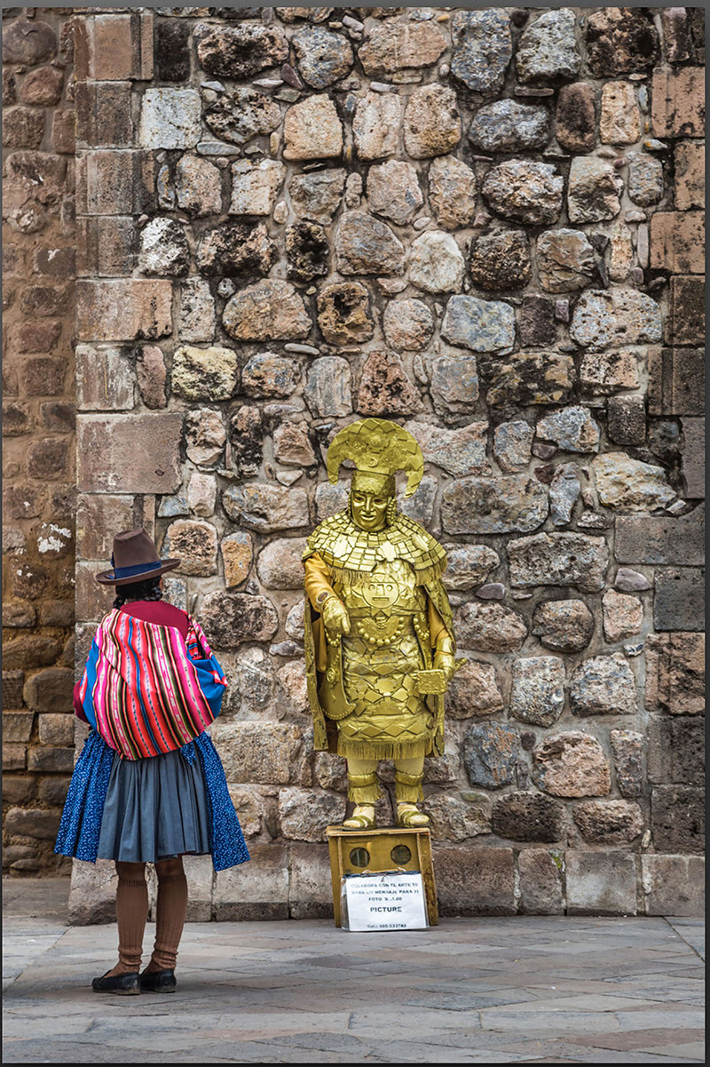 A photo of a street scene, with a stone wall background, a golden statue, and a figure in bright clothing