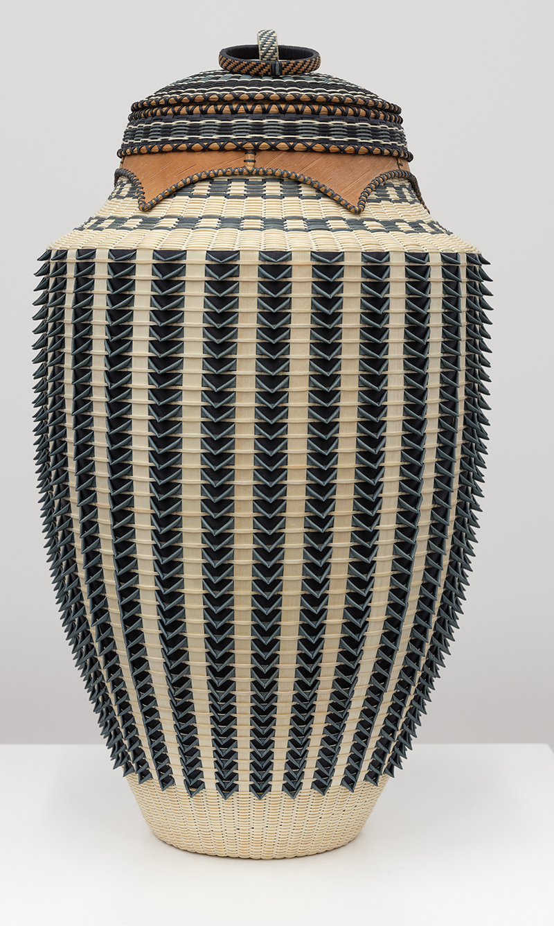 A vertical basket with cover with bold vertical striping in the weave