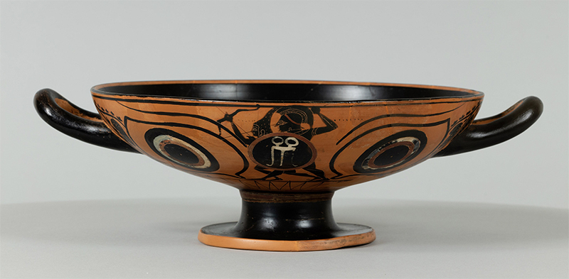 an ancient broad, shallow bowl with two handles on a pedestal vase, made of terracotta with black-figure painted decorative motifs