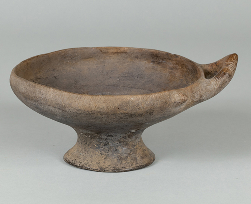 An ancient, dusty-colored clay, stem-footed bowl
