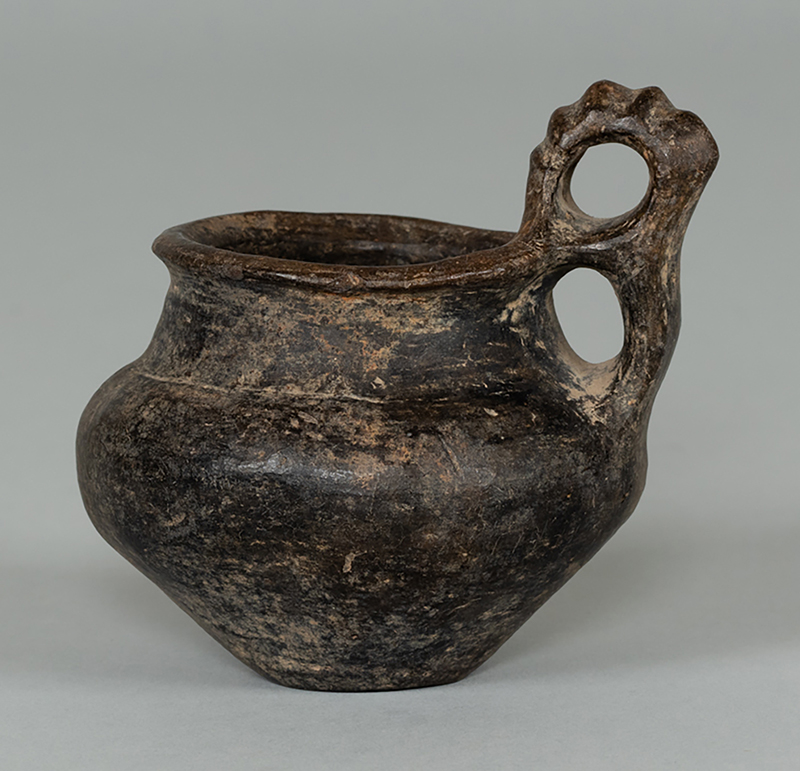 An ancient clay vessel that would hold water and has a fancy handle
