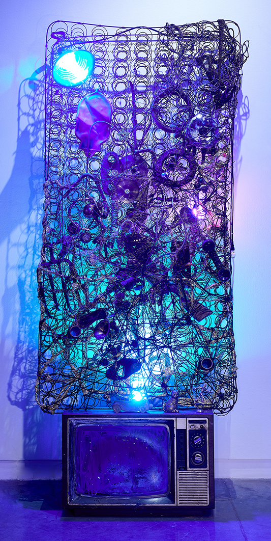 A sculpture with a metal bed frame with accumulated debris and lights.