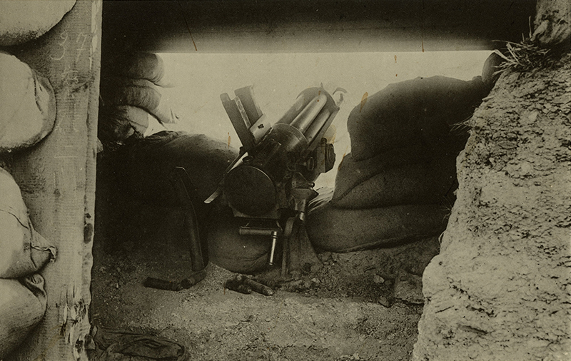 Sepia photograh of a large machine gun in a structure, nestled near bags of sand