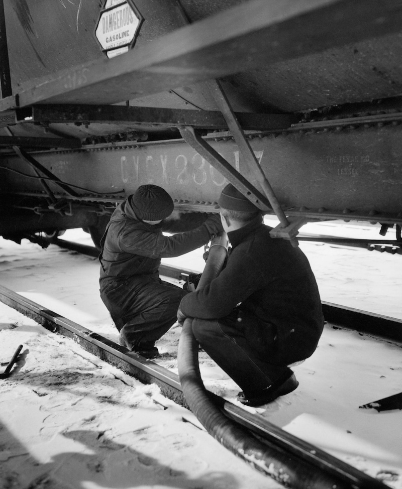 A black and white photograph two people fill up an airplane with gasoline