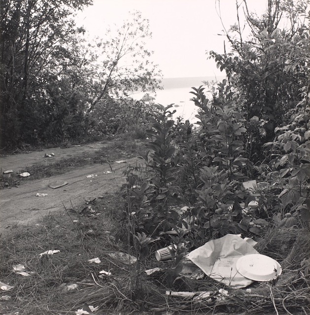 A black and white photograph shows trash littering a coastal landscape