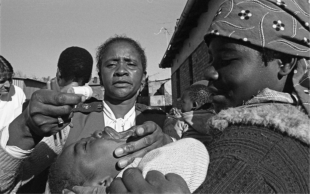 A black and white photograph depicts medicine being dropped into a child's mouth