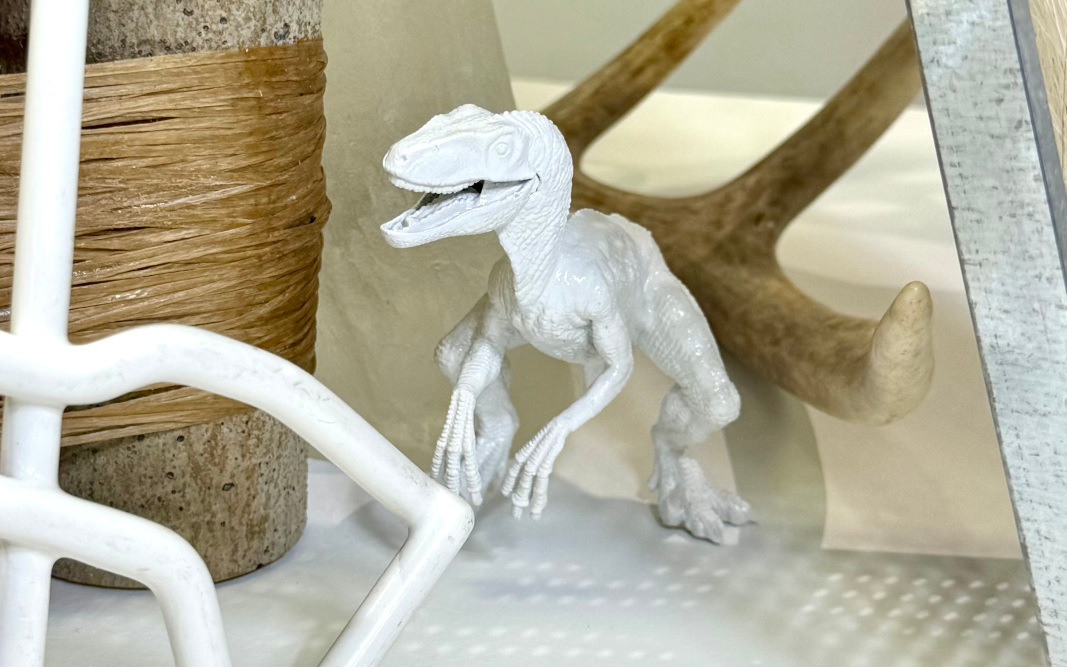 a dinosaur doll pears out from behind iron bars, with an antler behind it