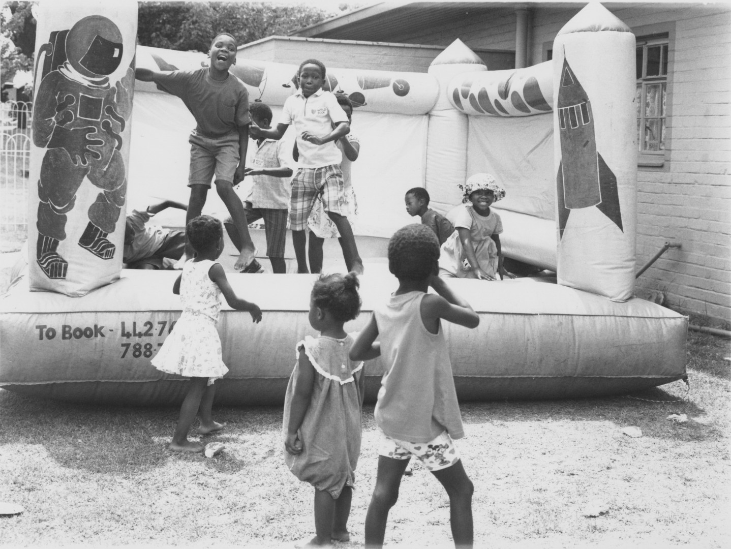 children play on an inflated funhouse. An astronaut and rocket are displayed on the side of the house.