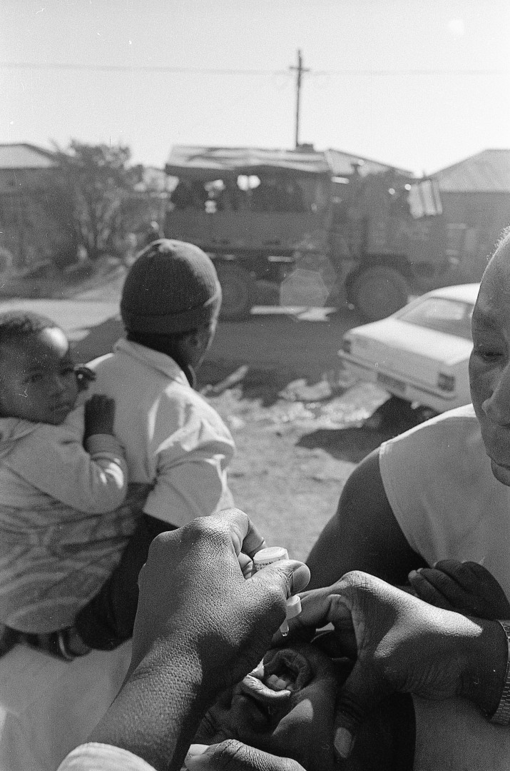 a woman holds a child while another woman administers oral medicine.