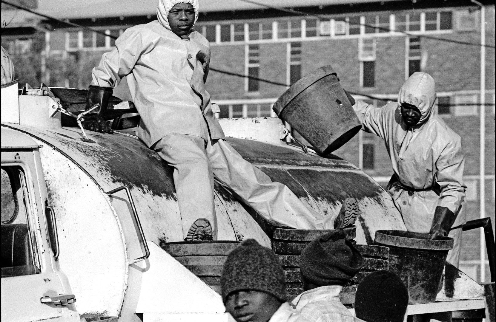 men in protective gear gather around a garbage truck.