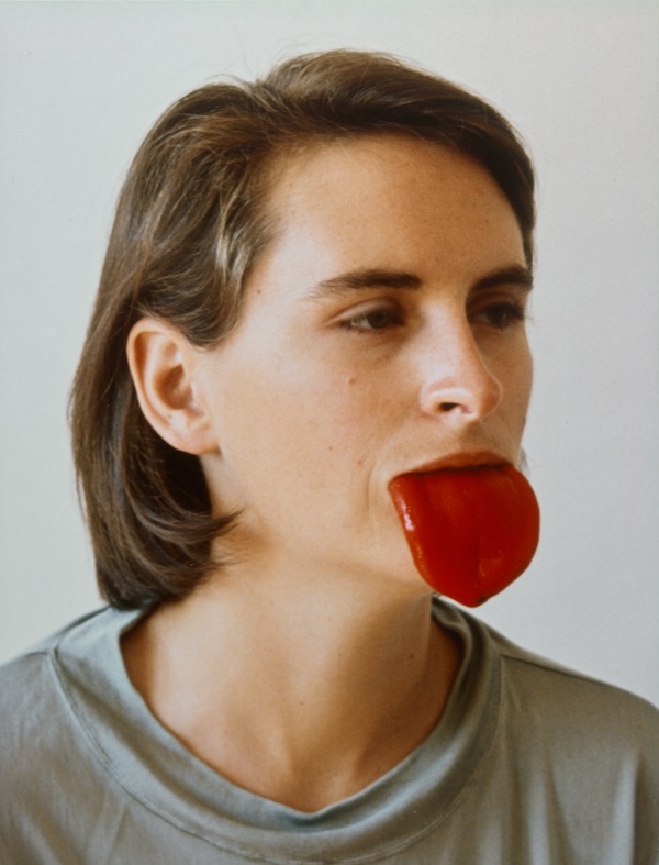 A color photograph of a person with a red pepper sticking out of their mouth like a tongue