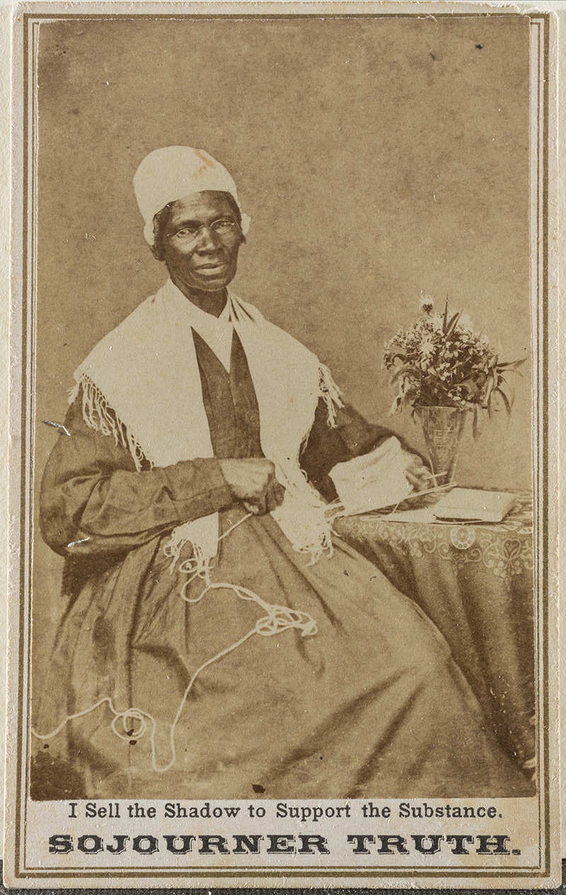 a sepia photograph showing a seated woman in a long dress with a shawl and cap