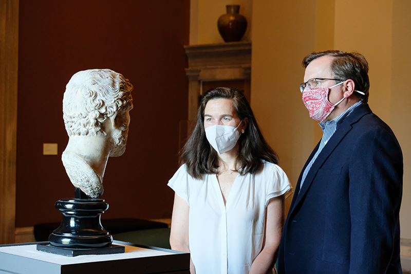 Two people in masks looking at an ancient sculpture