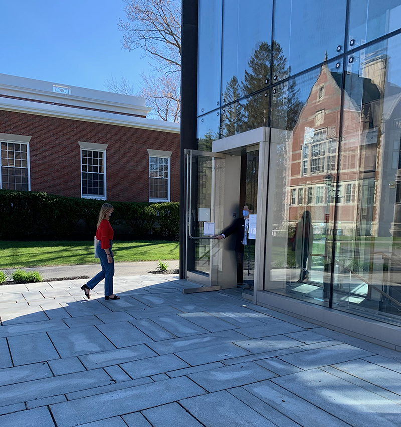 A  figure in a red shirt walking toward a building (pavilion) made of glass