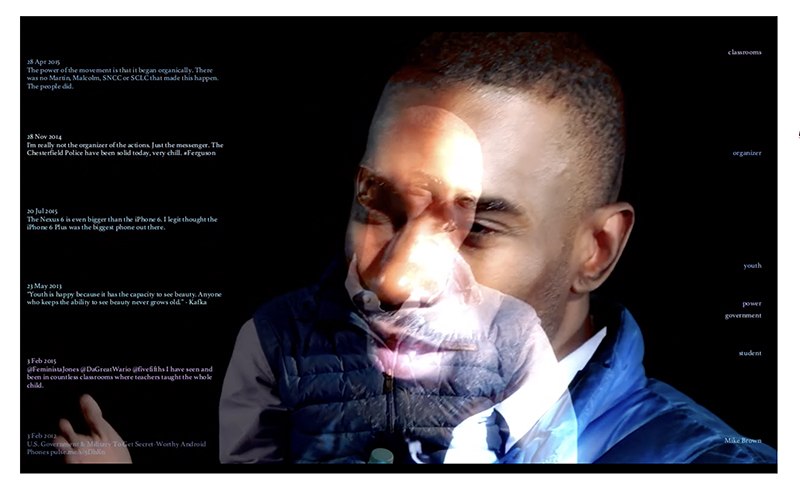 A close-up of a man's face, in front of a computer screen with lettering
