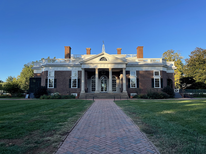A brick building with four white columns and four chimneys set at the end of a brick walkway