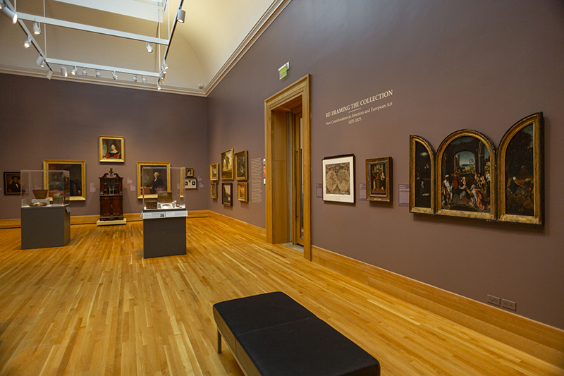 a view of a gallery with paintings on the walls and cases with objects in the center of the room