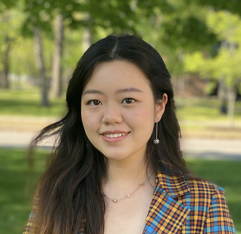 A photo of a woman with dark hair, wearing a plaid blazer