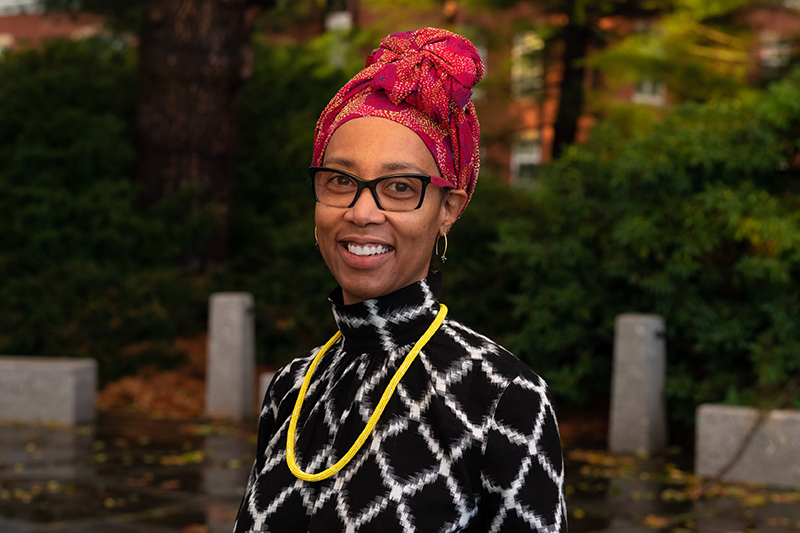 A photograph of a smiling woman with glasses and a red head covering