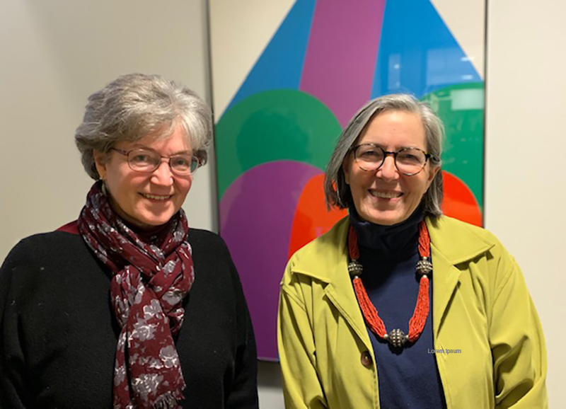 Two smiling women standing in front of an abstract poster