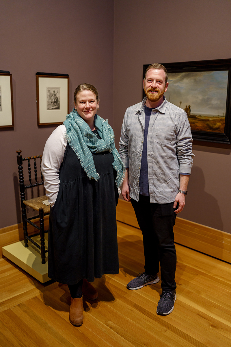 A woman with a flowing scarf and a man with a beard standing next to each other in an art gallery